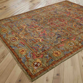 A traditional oriental area rug with an intricate floral pattern in muted tones of soft green, pale blue, honey, pink, and rust, shown laid out on a light wood plank floor.