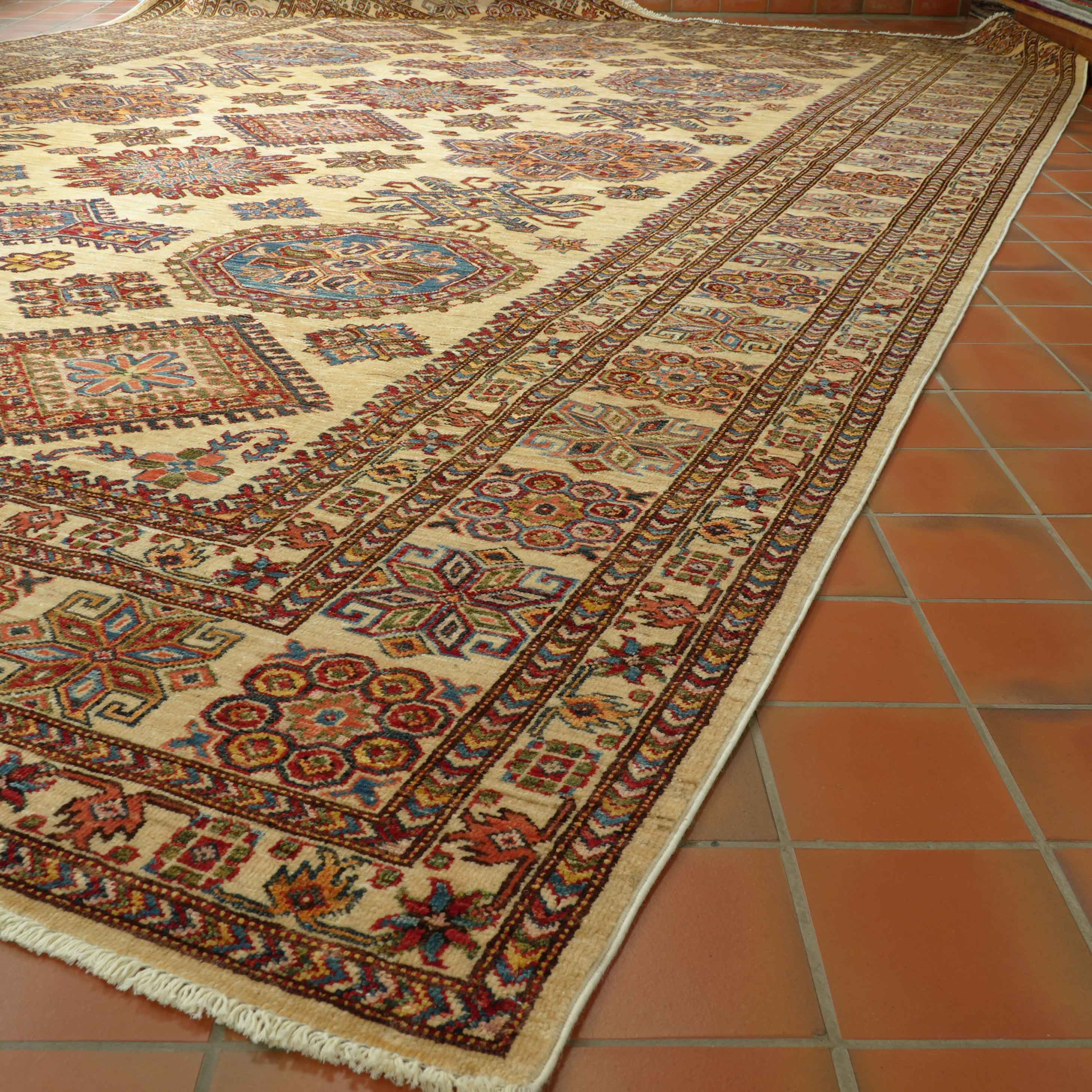 A handmade Afghan Kazak carpet with a geometric design, featuring a cream-colored background with red, green, and blue patterns, and a fringed edge.